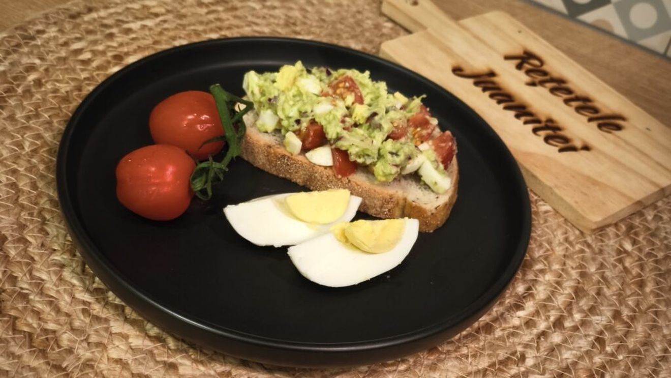 Avocado cu ouă, ceapă și roșii, totul întins pe o felie de pâine proaspătă sau un cracker crocant