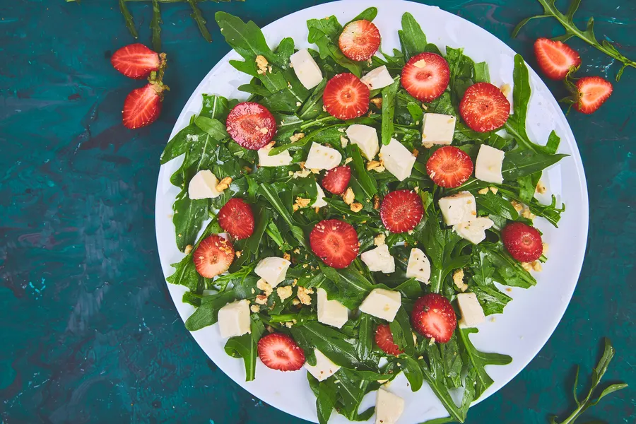 Fresh salad with arugula, strawberries, feta cheese and nuts on green background. Vegetarian. Diet food. Italian food. Top view. Copy space.